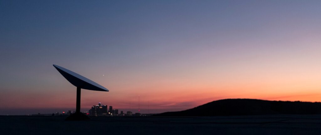 Starlink dish silhouetted against a dusk sky with a city skyline on the horizon