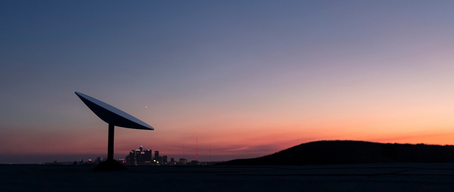 Starlink dish silhouetted against a dusk sky with a city skyline on the horizon